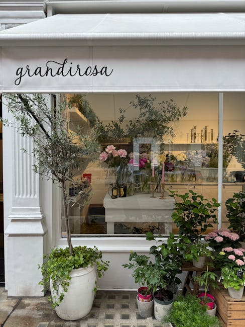 View of the exterior of Bermondsey Street florists, showcasing a large white awning with the word 'grandirosa' written in black cursive. Through the glass window, an interior space is visible, decorat