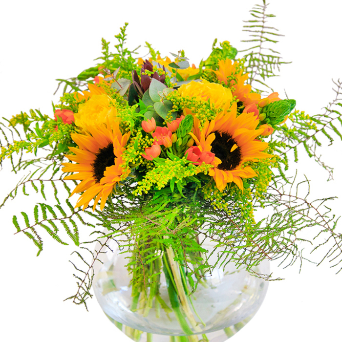 This intricately balanced bouquet is a radiant tribute to Bermondsey's modern flair and welcoming neighbourhood charm. Standing tall, sunflowers with deep caramel centers and glowing golden petals form a striking focus, their joyful energy reminiscent of weekend mornings along Bermondsey's bustling riverside paths. Nestled beside them, pale yellow garden roses show off tightly packed spirals of petals, each catching the light with luminous softness. Glossy red Hypericum berries sparkle amid an abundance of feathery fern fronds and slender spikes of yellow solidago, their playful forms echoing the movement found in local parks after the rain. Flecks of eucalyptus, tinged with blue-green, weave subtle harmony through the arrangement, their scent as gentle and refreshing as a breeze by Southwark Park. All are arranged in a pristine, spherical glass vase, the submerged stems and pure water reflecting the thoughtful, transparent beauty prized by Bermondsey Florist. The overall mood is one of celebration-perfect for birthdays, anniversaries, or sending a cheerful message to friends and loved ones throughout the area, with every petal and stem chosen to reflect the area's blend of heritage and new beginnings.